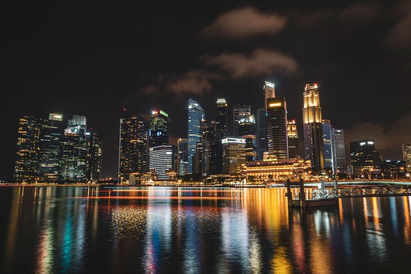 The Singapore skyline lit up at night, with colourful reflections across Marina Bay