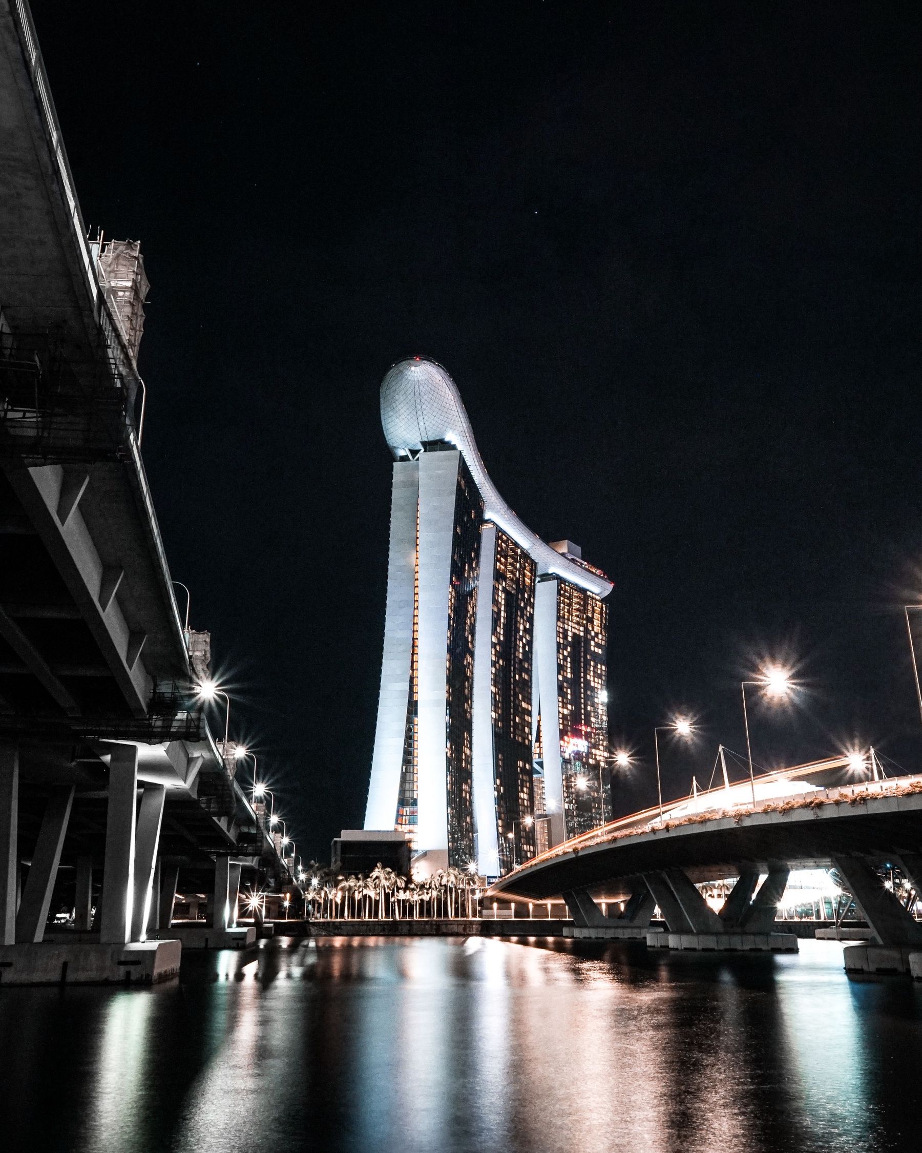 Marina Bay Sands seen between two bridges, reflected in the water at night