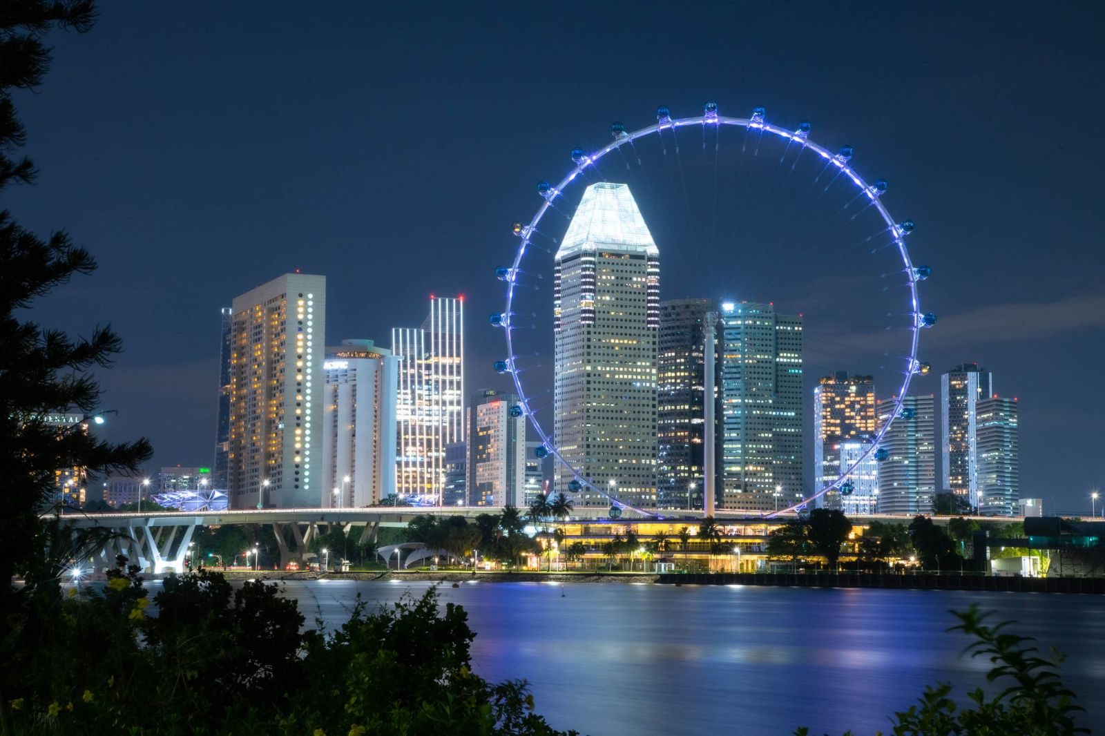 Illuminated Singapore skyline and Ferris wheel reflecting over the water at night.