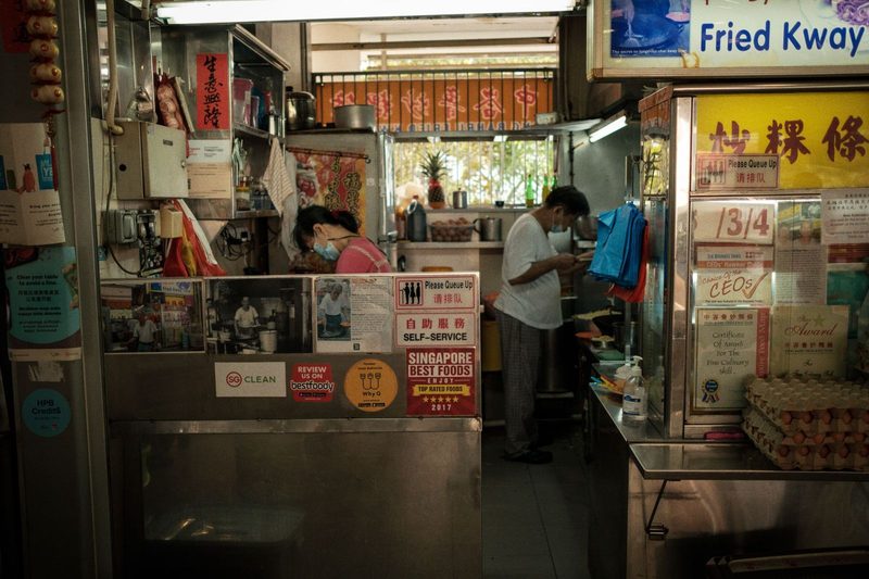 A bustling hawker stall in Singapore with staff preparing food in a vibrant setting.