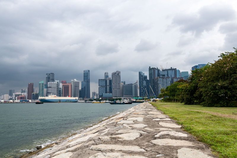 A vibrant Singapore skyline overlooking the calm sea with an adjacent paved path.