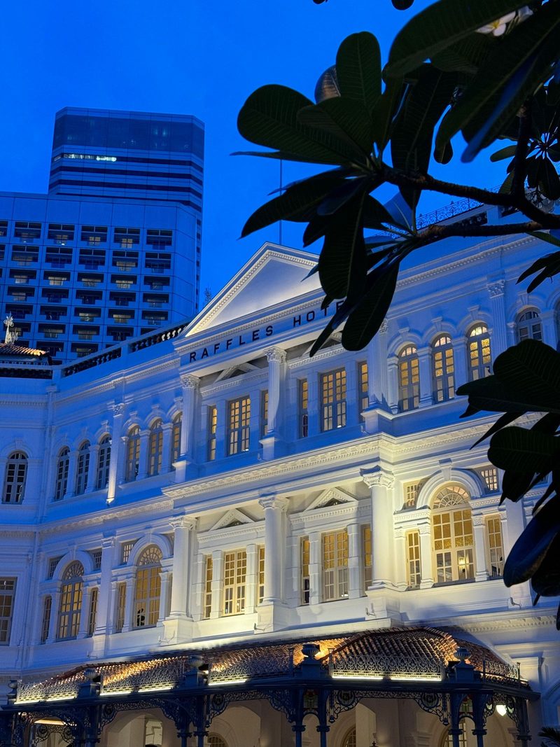 Elegant view of Raffles Hotel in Singapore illuminated against a twilight sky.