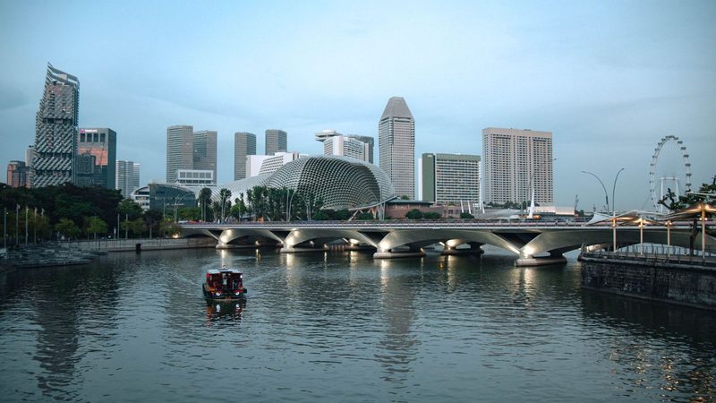 Evening view of the Singapore cityscape featuring a bridge over the river and iconic landmarks.