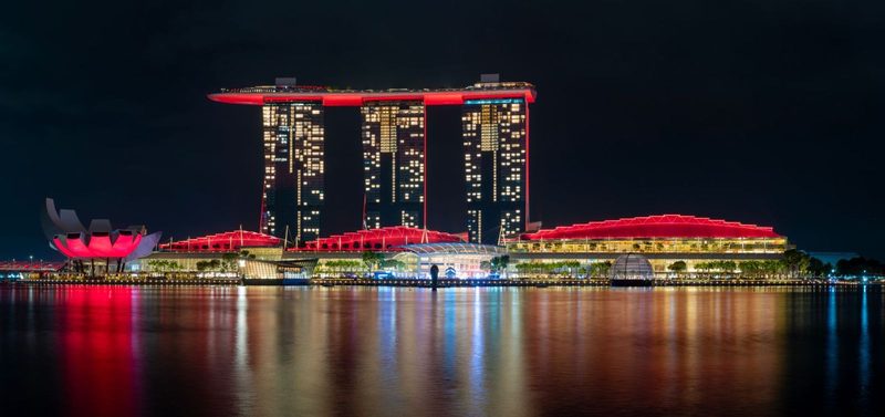 Stunning night view of Marina Bay Sands with vibrant red lighting reflecting on the water.