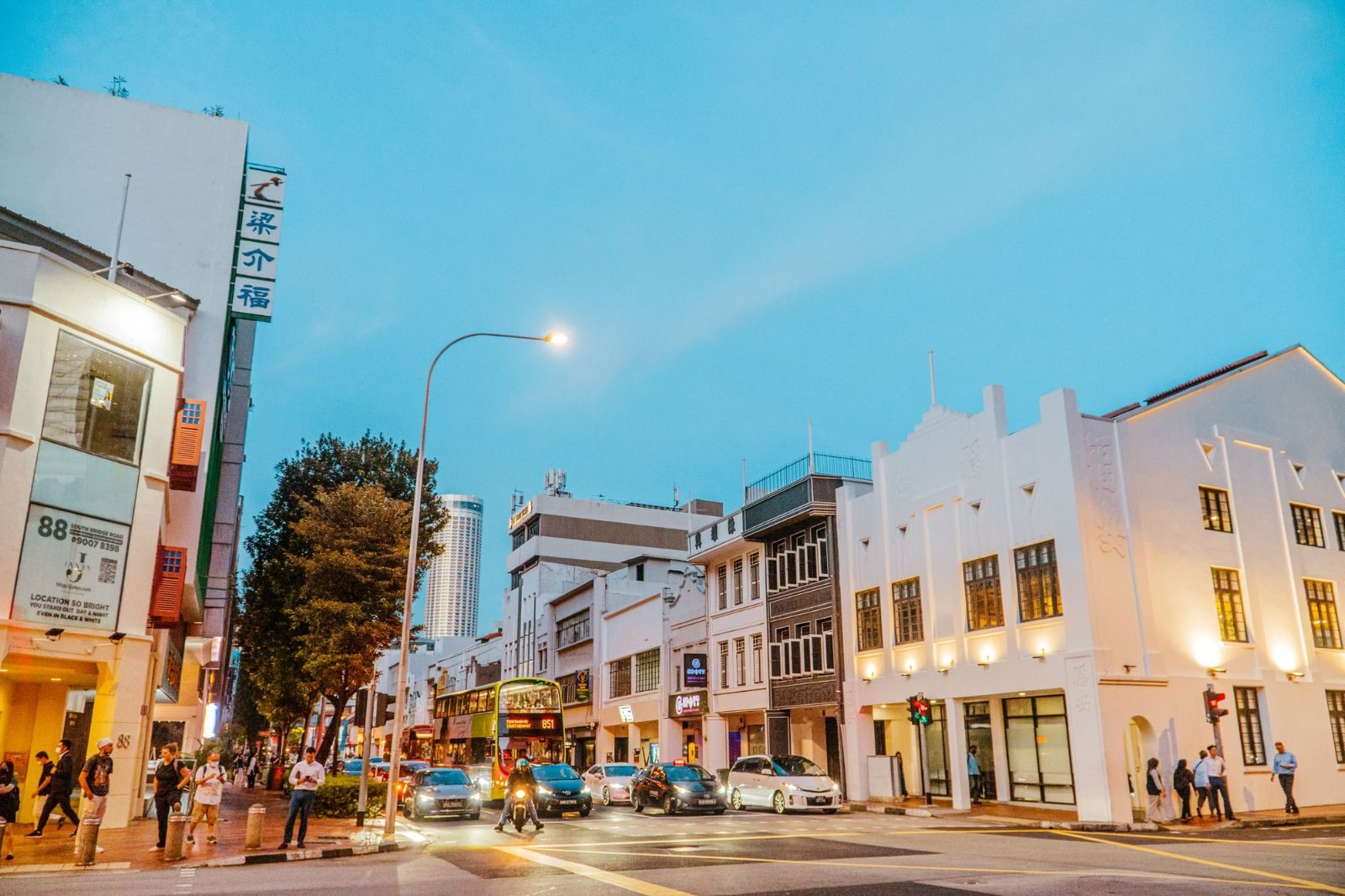 Bustling street in Singapore with colonial architecture and lively atmosphere at dusk.