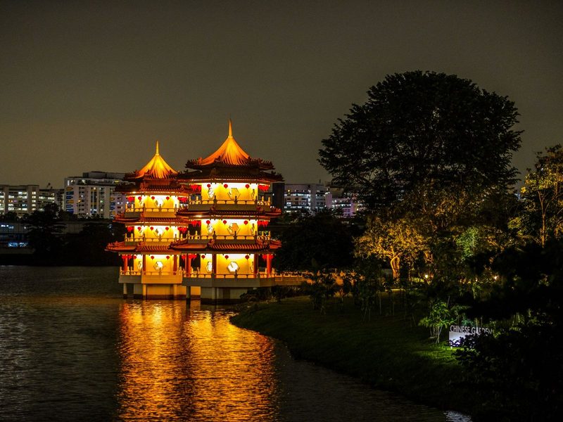 A glowing pagoda reflected in water at night in a serene Chinese garden setting.