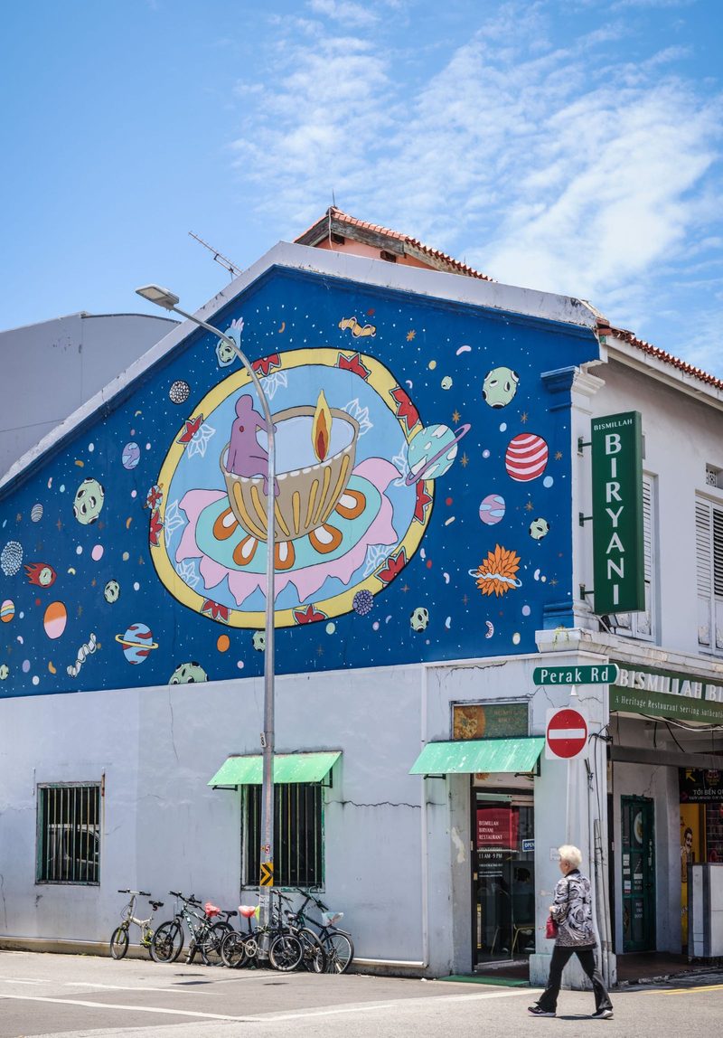 Vibrant street art mural on building corner with a passerby in urban setting.