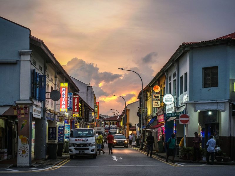 Busy street with colorful shops and vehicles at sunset, capturing urban life and vibrant atmosphere.