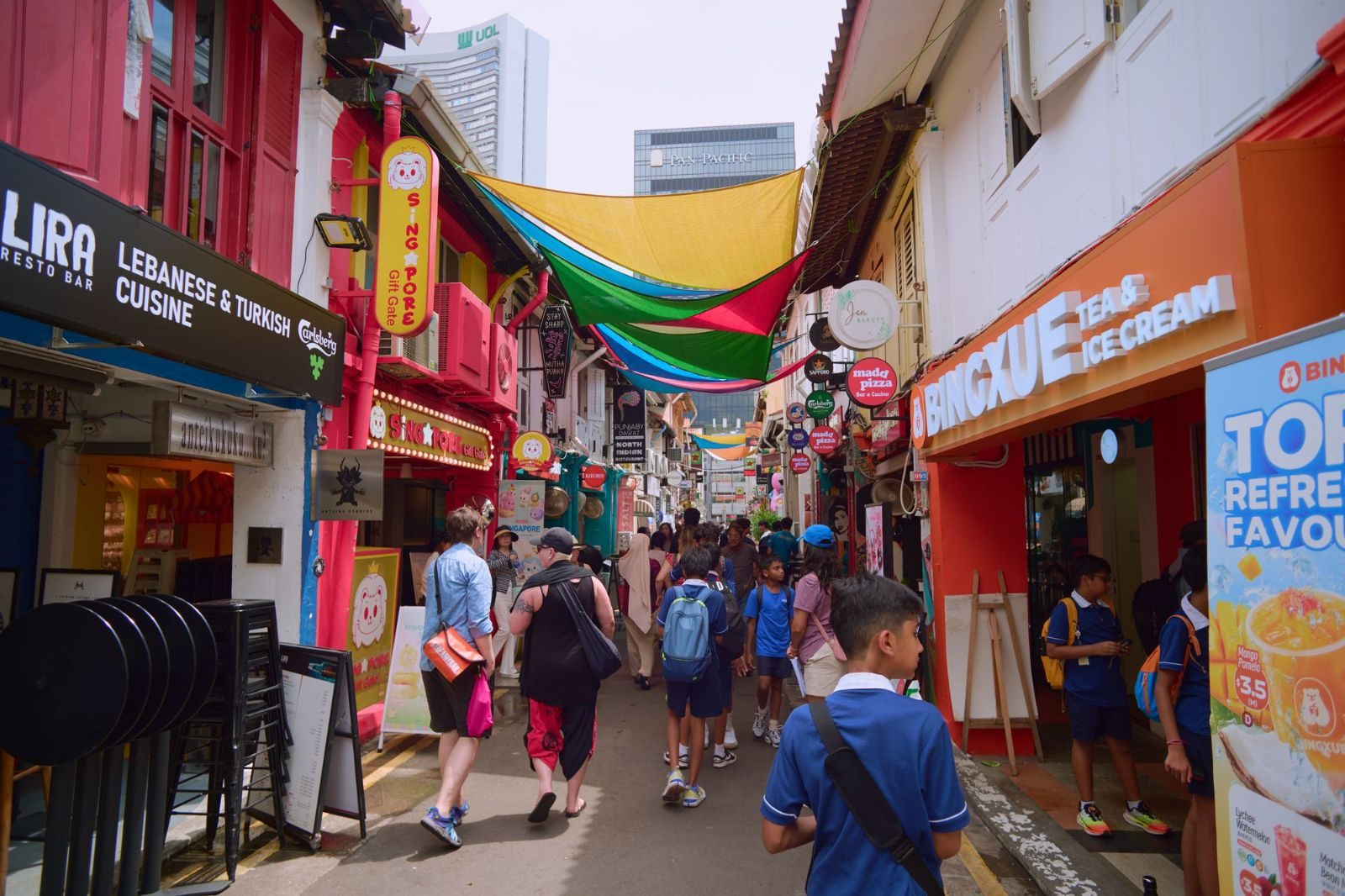 A bustling and colorful street scene in Singapore's Haji Lane featuring diverse shops and people.