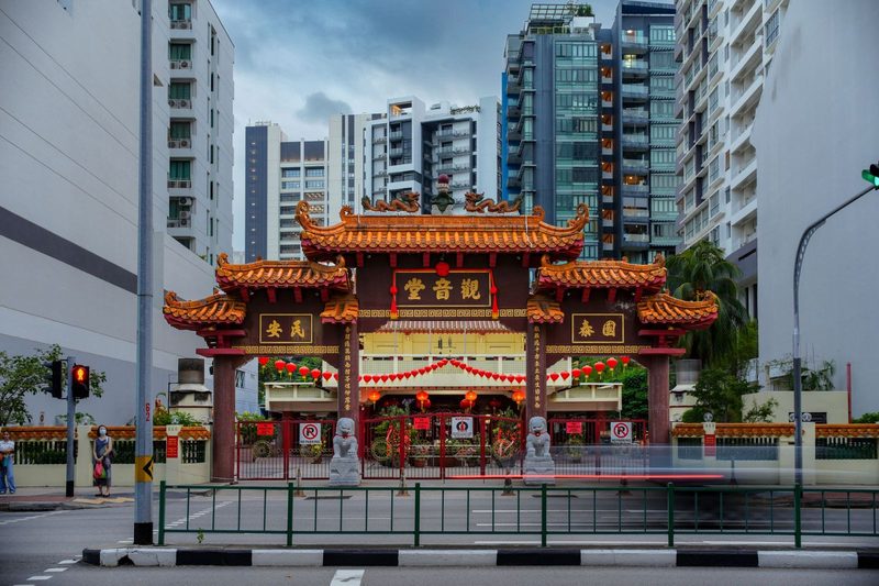 Traditional Chinese temple gate surrounded by modern urban buildings at twilight, highlighting cultural juxtaposition.