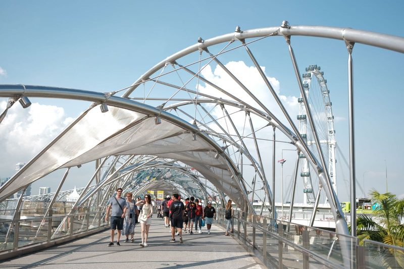 Visitors stroll along Singapore's iconic Helix Bridge with the city skyline and Singapore Flyer in view.