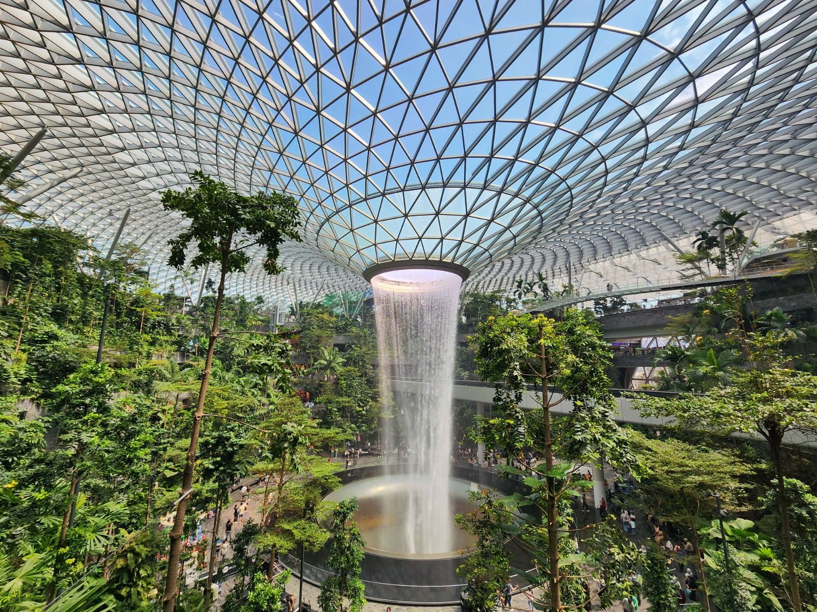 Stunning indoor waterfall at Jewel Changi Airport with lush greenery and glass dome.