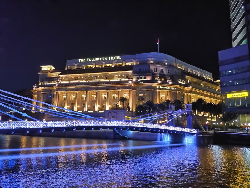 Illuminated Fullerton Hotel and Cavenagh Bridge reflecting on water at night.