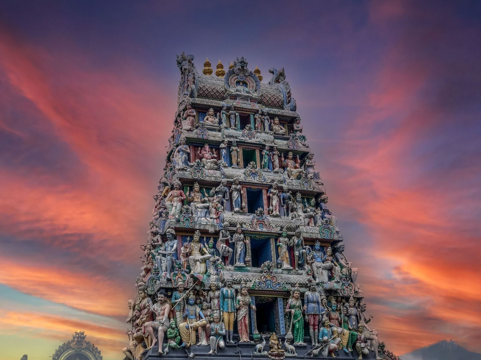 Sri Mariamman Temple in Singapore with a vibrant sunset sky, displaying intricate carvings.