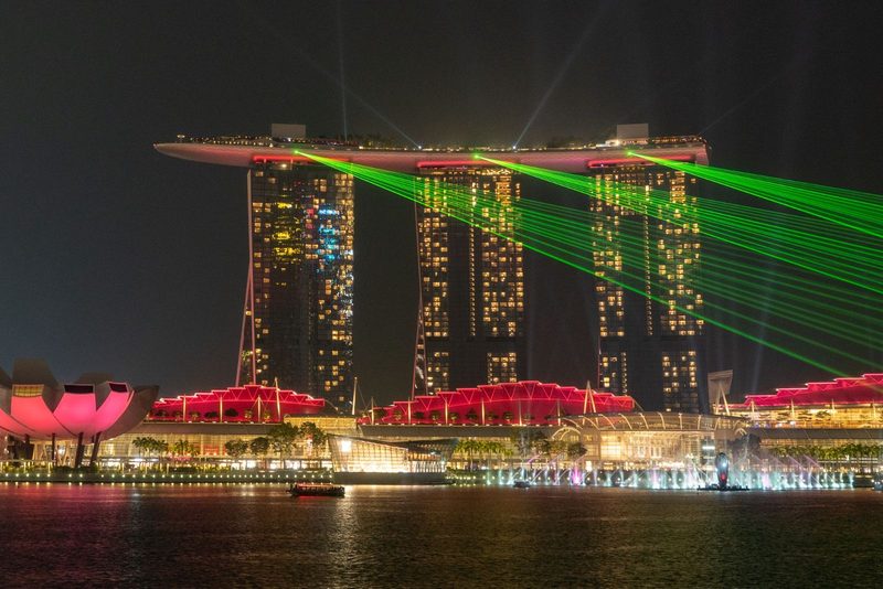 A stunning view of Marina Bay Sands with vibrant laser lights illuminating the Singapore skyline at night.