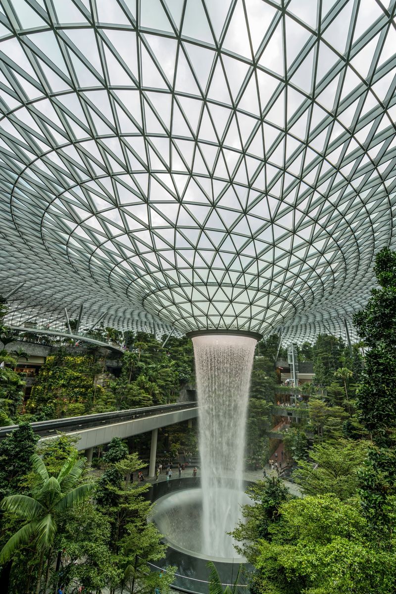The Rain Vortex falling through the glass dome of Jewel Changi, surrounded by trees